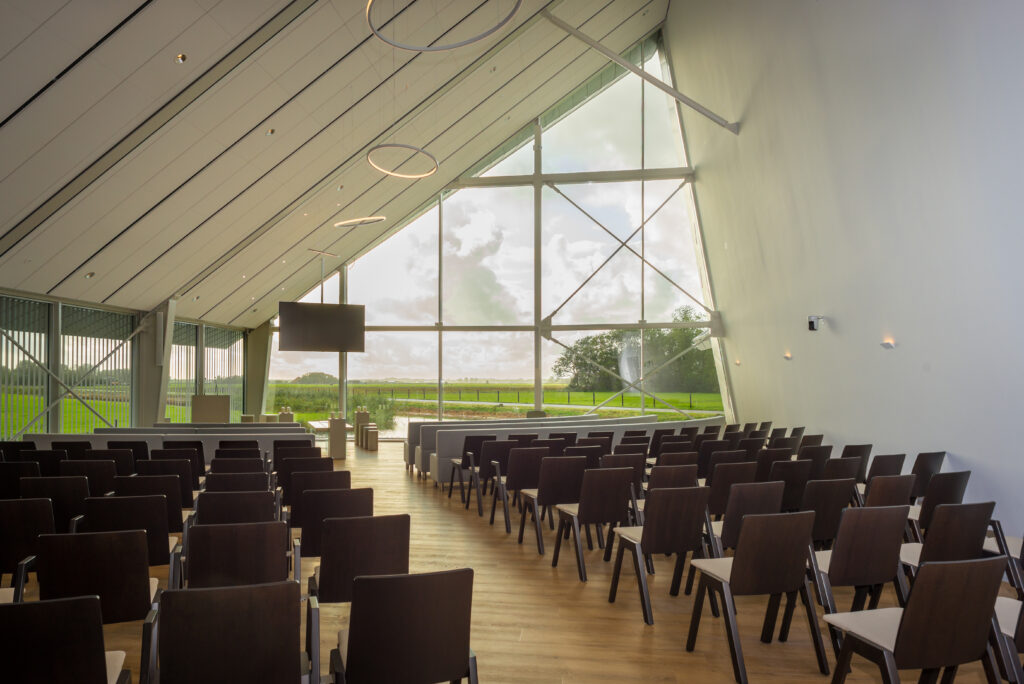 De aula van Crematorium Alkmaar, met stoelen op rij en een glaswand met uitzicht over de polder