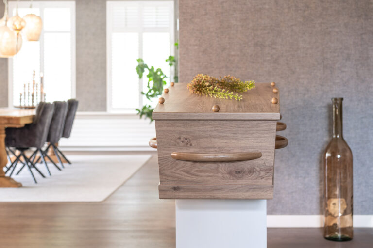 Houten uitvaartkist met een takje groen op het deksel, opgebaard in een woonkamer